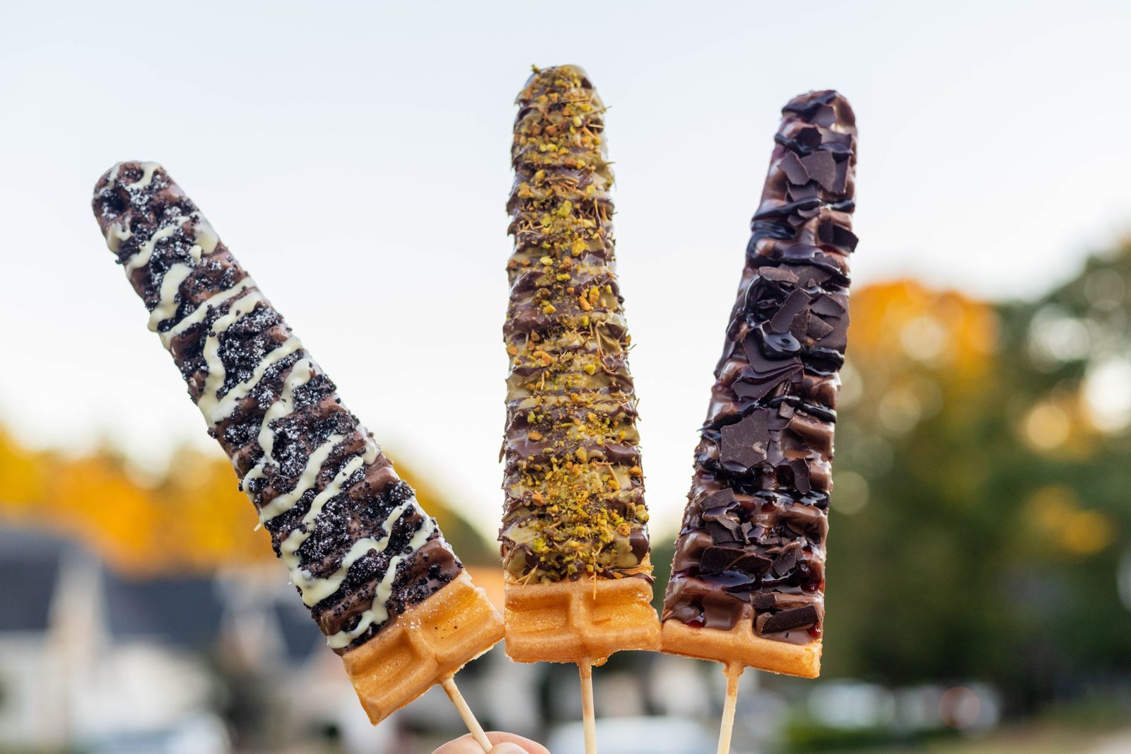 Oreo Snowstorm, Dubai Chocolate and Black Forest waffle wands held up outdoors